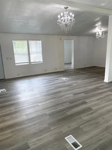 an empty room with wooden floor chandelier and windows