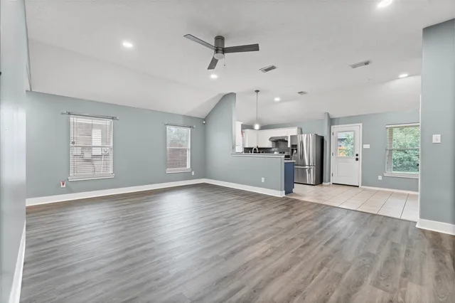 an empty room with wooden floor a kitchen view and windows