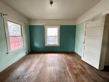 an empty room with wooden floor closet and windows