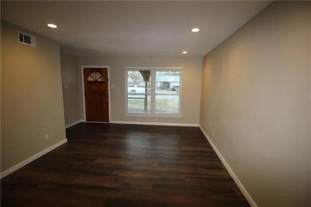 an empty room with wooden floor and windows with curtains