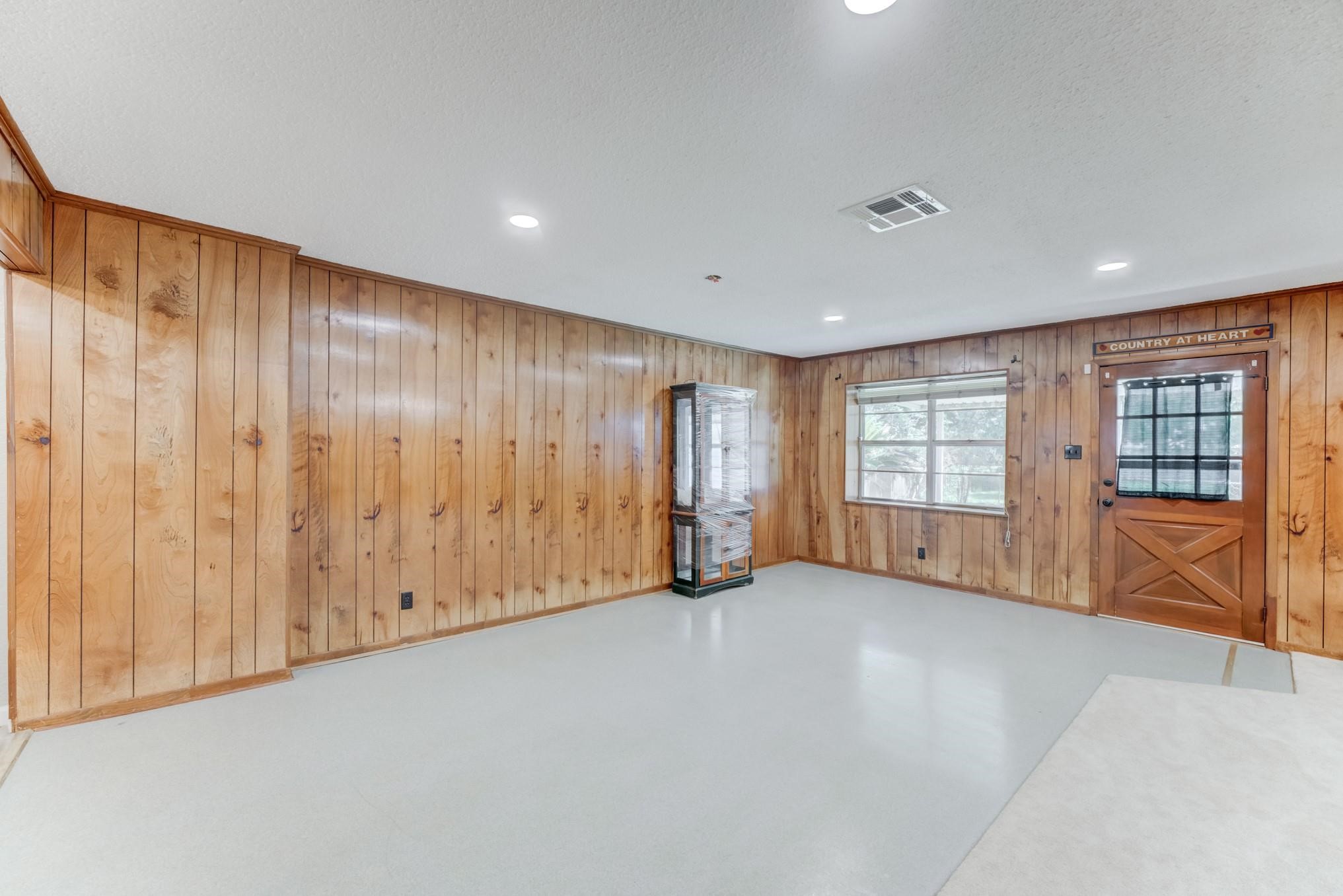 305 Yaupon Street Sweeny, TX 77480 - Photo 9 of 22 This room features classic wood paneling, a window for natural light, and a wooden door with a decorative glass insert. The open space is versatile for various uses.