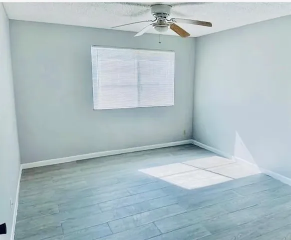 an empty room with wooden floor chandelier fan and windows