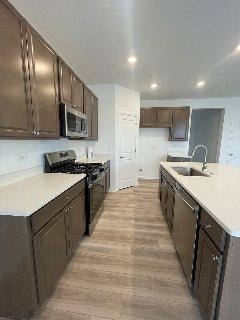 104 Henderson Street Oswego, IL 60543 - Photo 7 of 21 a kitchen with stainless steel appliances granite countertop a sink and dishwasher a stove top oven with wooden floor