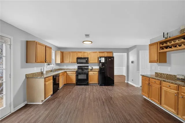 a large kitchen with stainless steel appliances granite countertop a stove top oven a sink dishwasher and a refrigerator with wooden floor