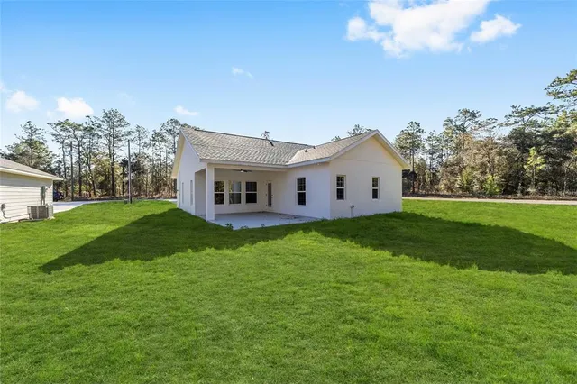 a view of a white house in front of a big yard with plants and large trees