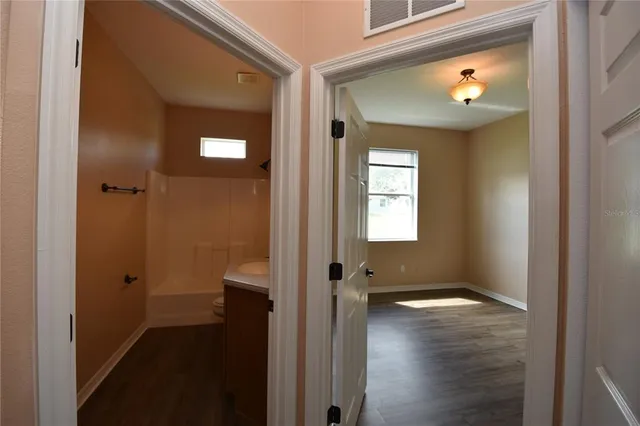 a view of a hallway with wooden floor and a bathroom