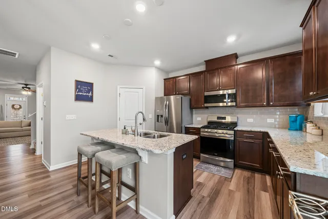 a kitchen with stainless steel appliances granite countertop a stove top oven a sink dishwasher a dining table and chairs with wooden floor