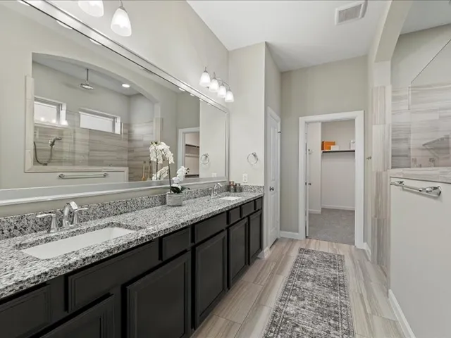 a bathroom with a granite countertop double vanity sink a mirror and shower