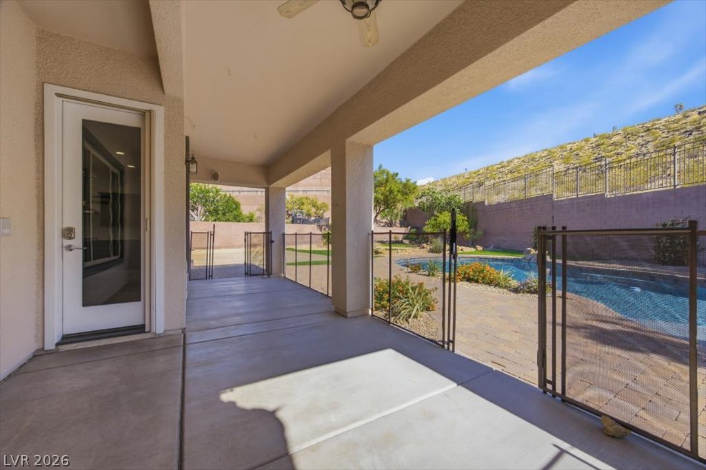 2125 De Rouge Avenue Henderson, NV 89044 - Photo 69 of 96 Step out to a covered patio leading to a fenced pool area, set against a desert landscape.