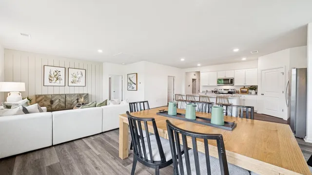 a living room with stainless steel appliances a dining table wooden floor and a kitchen view
