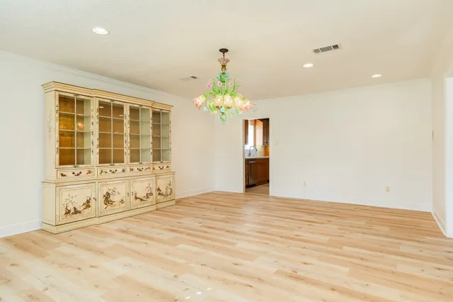 a view of an empty room with chandelier and wooden floor