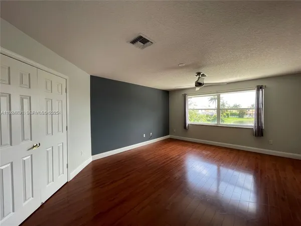 an empty room with wooden floor chandelier fan and windows