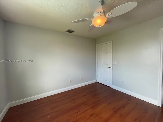 an empty room with wooden floor ceiling fan and windows