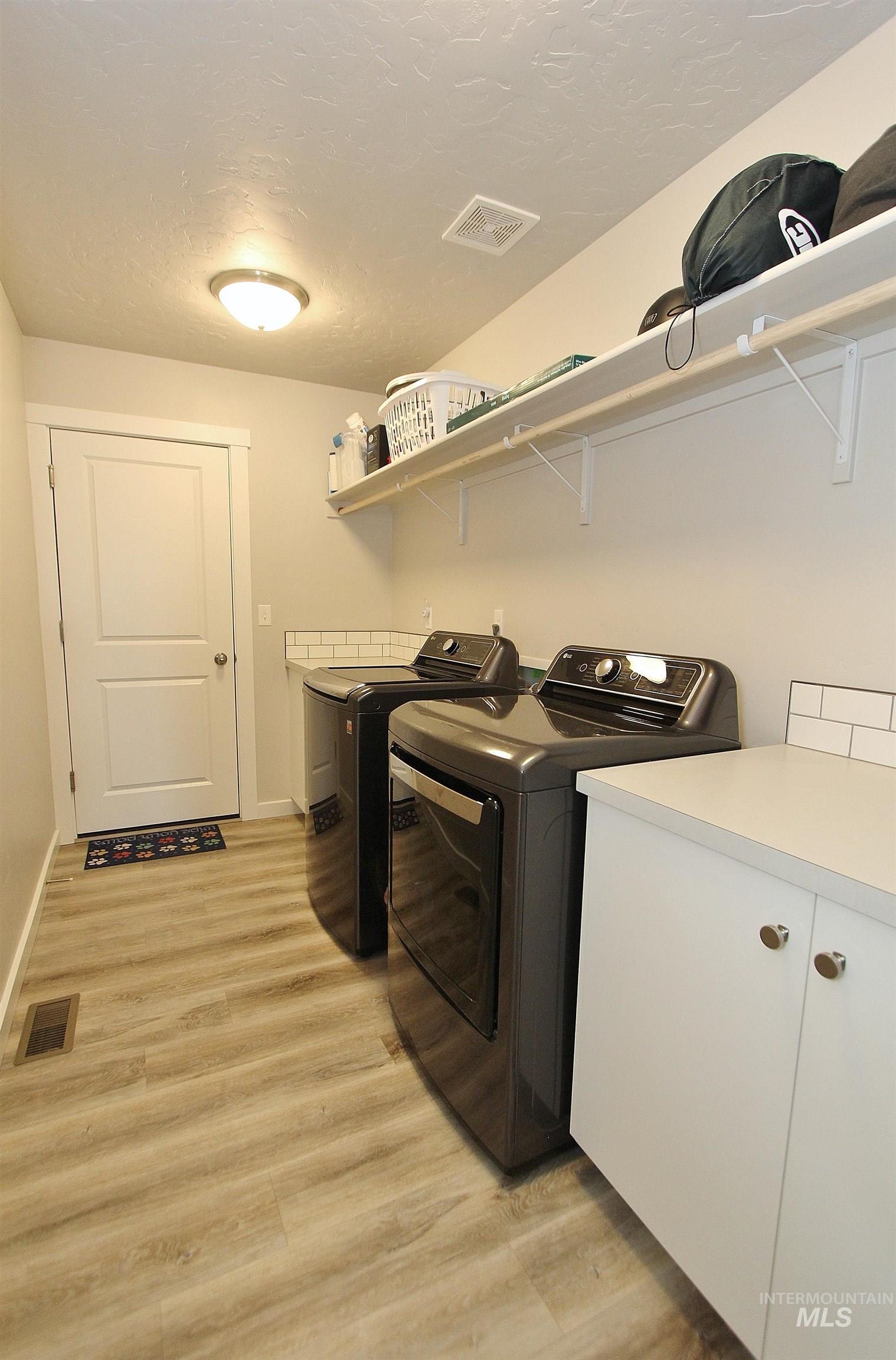 1211 Mahogany Street Parma, ID 83660 - Photo 18 of 22 Laundry area with light wood-type flooring, a textured ceiling, cabinet space, and washing machine and dryer