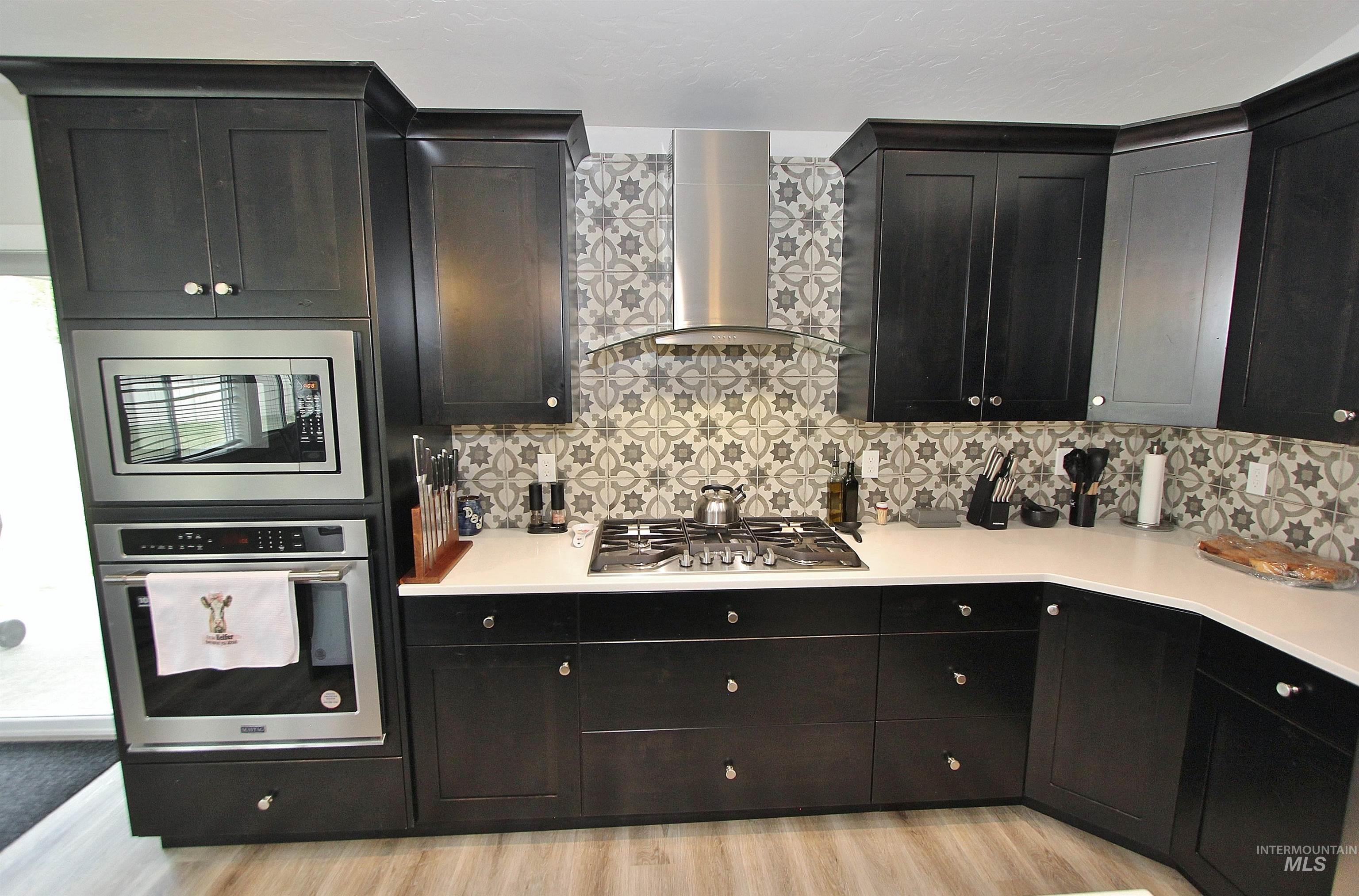 1211 Mahogany Street Parma, ID 83660 - Photo 7 of 22 Kitchen with stainless steel appliances, dark cabinets, light wood finished floors, and tasteful backsplash