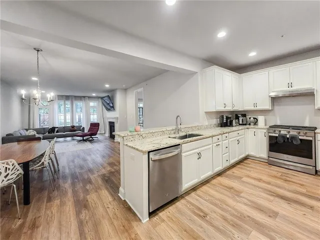 a kitchen with stainless steel appliances granite countertop a stove top oven a sink dishwasher a refrigerator and white cabinets with wooden floor