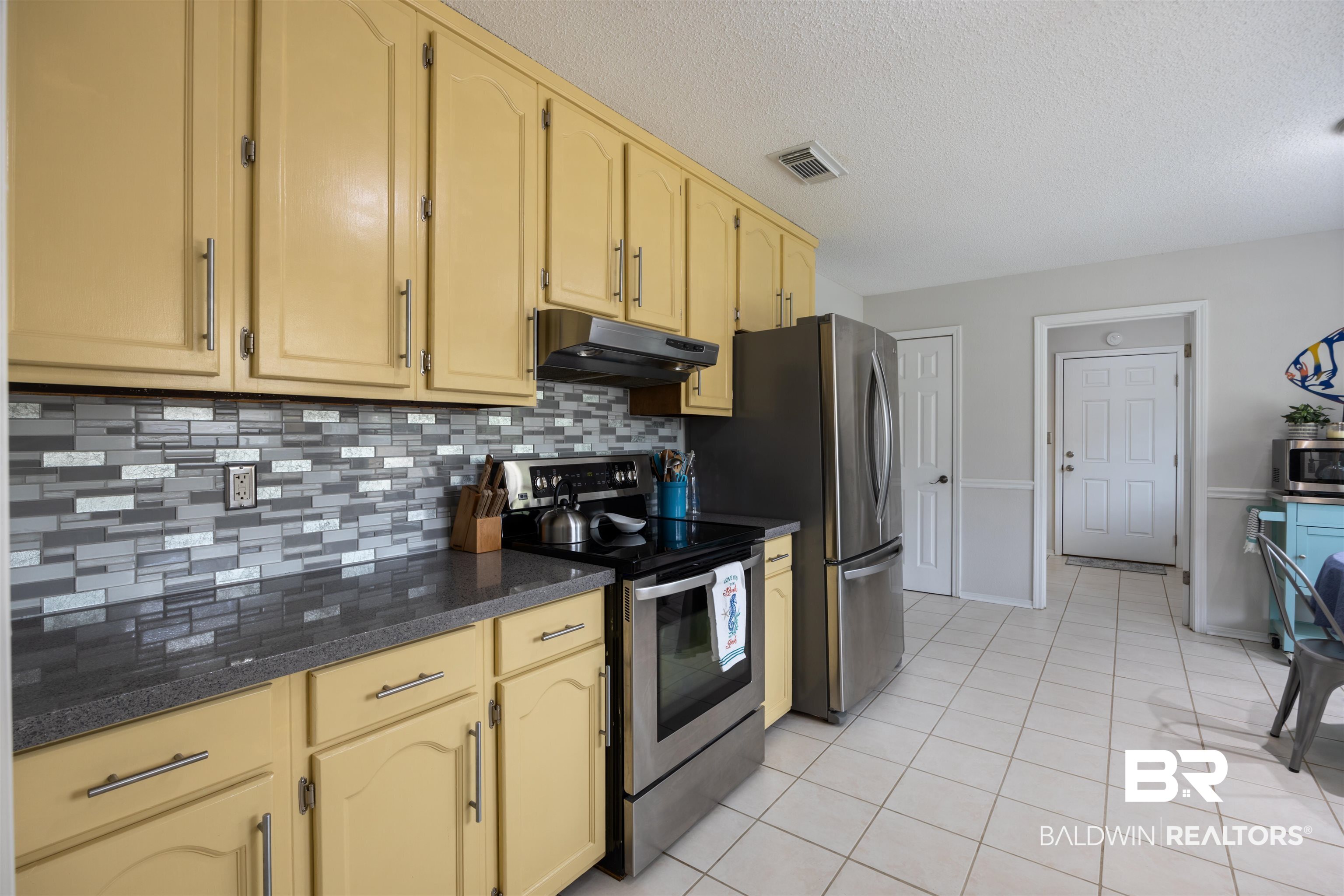 9771 Clarke Ridge Road Foley, AL 36535 - Photo 38 of 72 Kitchen with under-cabinet range hood, light tile patterned floors, visible vents, tasteful backsplash, and appliances with stainless steel finishes.