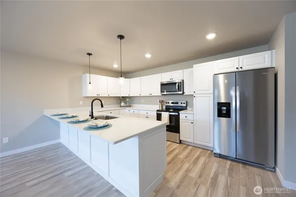a kitchen with stainless steel appliances granite countertop a refrigerator a sink dishwasher a stove with white cabinets and wooden floor