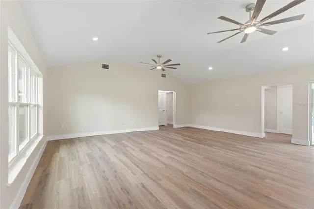 an empty room with wooden floor fan and windows