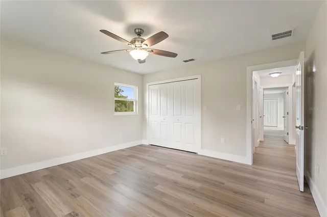 a view of an empty room with wooden floor and a ceiling fan