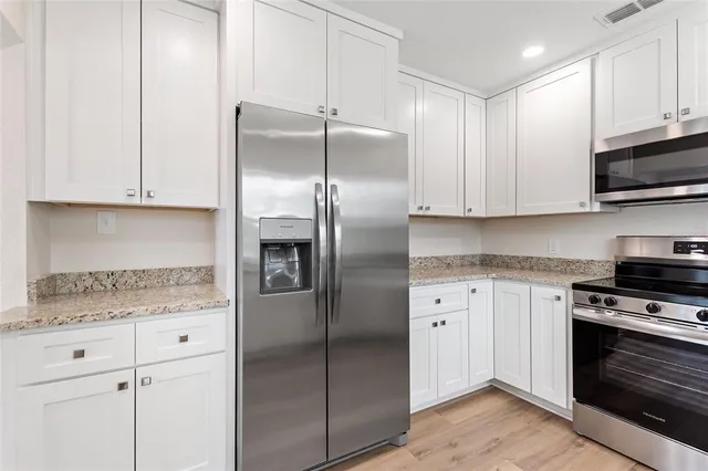 a kitchen with stainless steel appliances granite countertop a refrigerator a stove and white cabinets