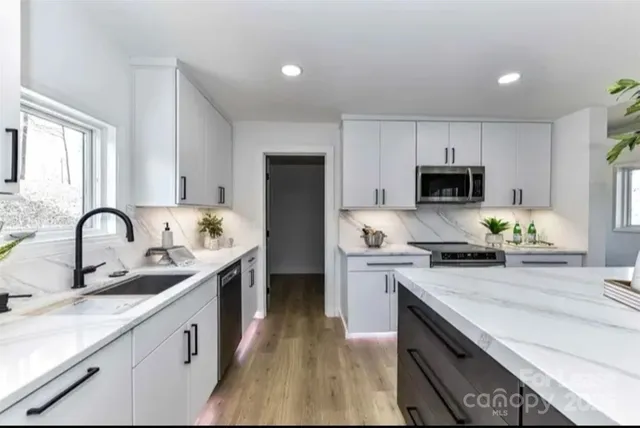 a kitchen with granite countertop a sink stainless steel appliances and white cabinets