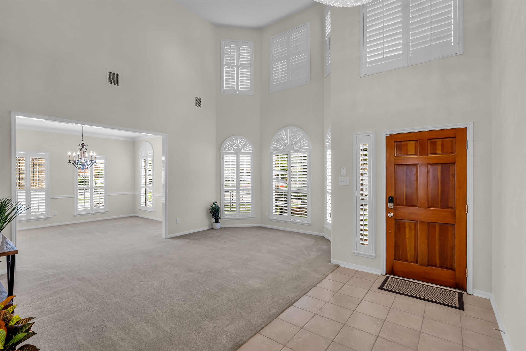 6807 Chapelfield Lane Houston, TX 77049 - Photo 5 of 42 This spacious entryway features high ceilings and ample natural light from large windows with elegant shutters. The area is tiled near the door, transitioning to carpet in the adjoining room, which is highlighted by a stylish chandelier.
