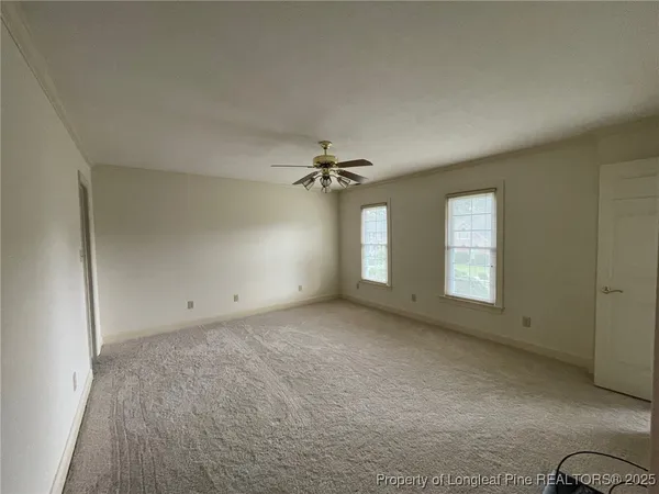 an empty room with chandelier fan and windows