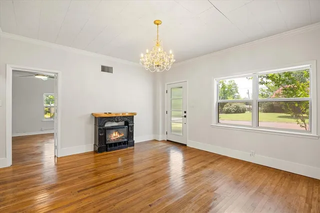 an empty room with wooden floor chandelier and windows
