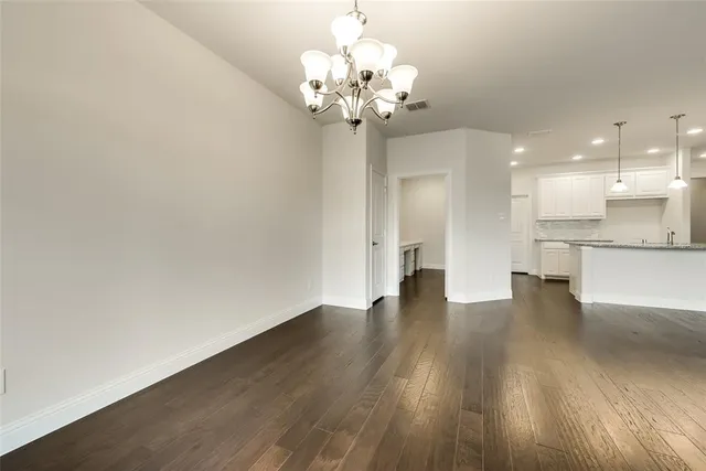 a view of an empty room with wooden floor and a kitchen