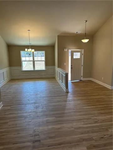 an empty room with wooden floor chandelier and windows