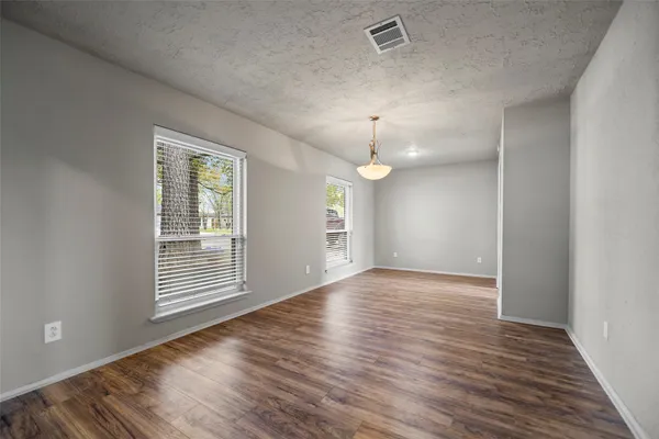 an empty room with wooden floor chandelier and windows