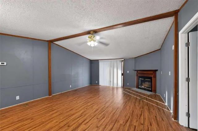 a view of an empty room with wooden floor fireplace and a window