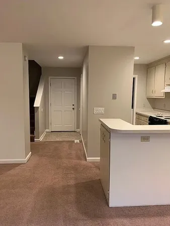 a view of an empty room with kitchen and window