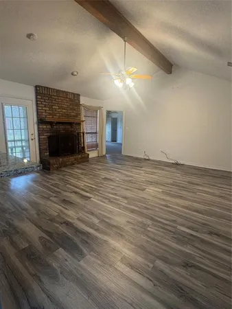 an empty room with wooden floor fireplace and windows