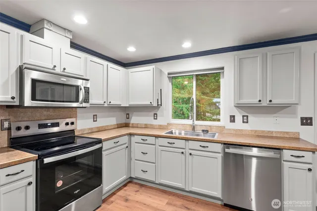a kitchen with granite countertop white cabinets appliances a sink and a window