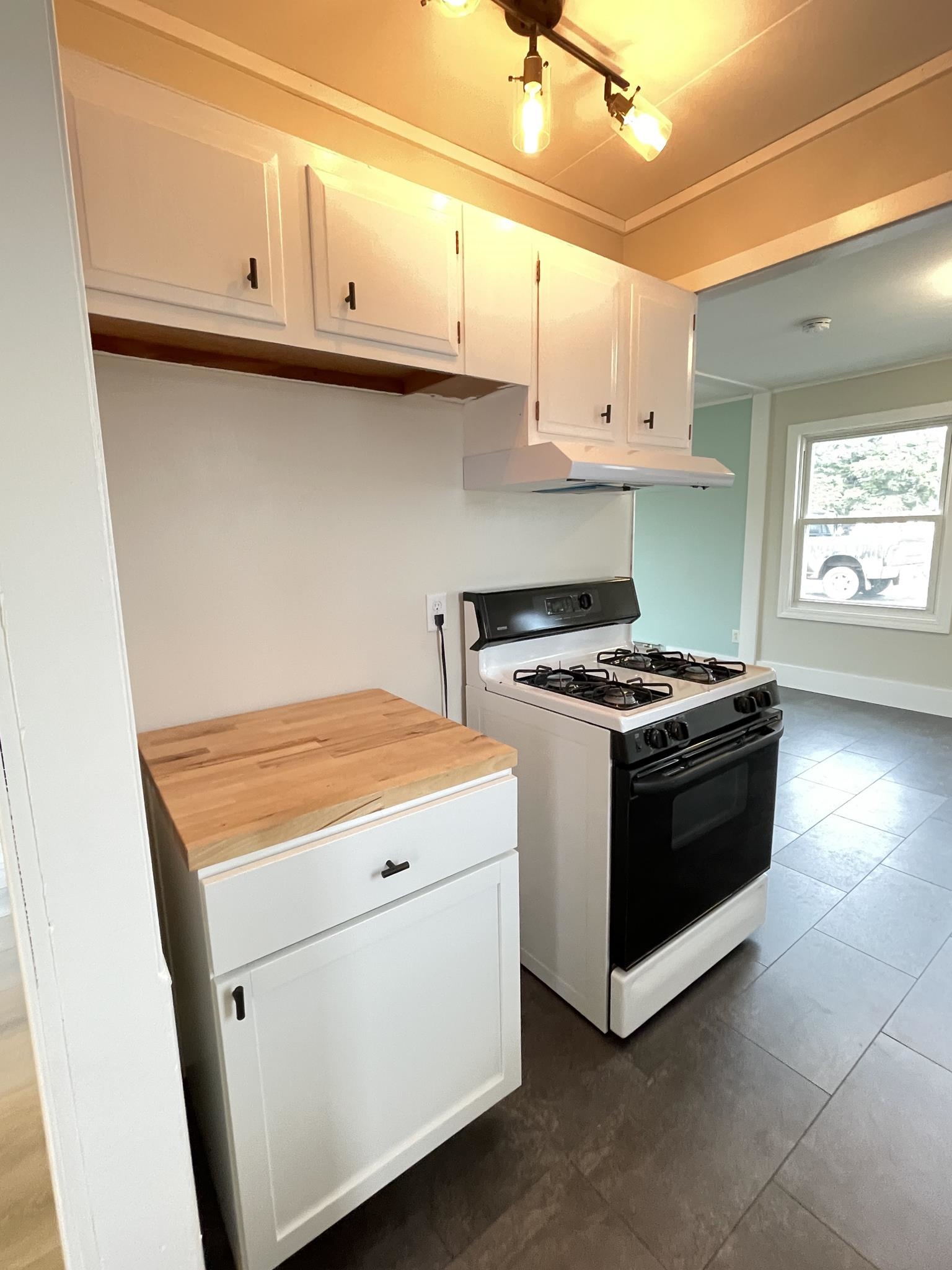 53 Edwards Drive Silver Bay, MN 55614 - Photo 9 of 30 Kitchen with white gas stove, white cabinetry, wooden counters, under cabinet range hood, and dark tile patterned flooring