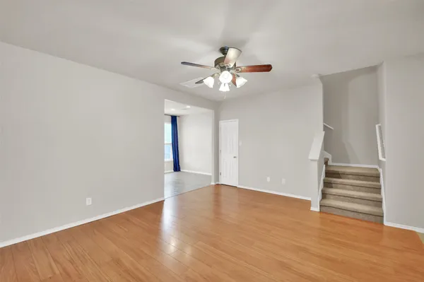 a view of an empty room with wooden floor and a ceiling fan