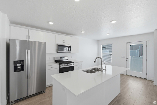 3788 South Galatia Road Magna, UT 84044 - Photo 8 of 24 Modern kitchen featuring a central island with an undermount double sink, stainless steel appliances, white cabinetry, recessed lighting, and wood-finish flooring
