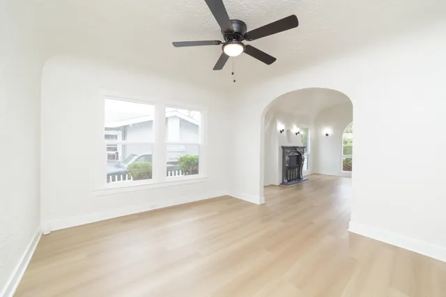 an empty room with wooden floor fan and windows