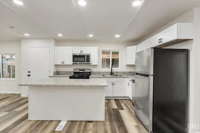 a kitchen with stainless steel appliances kitchen island granite countertop a refrigerator a stove top oven a sink dishwasher and white cabinets with wooden floor