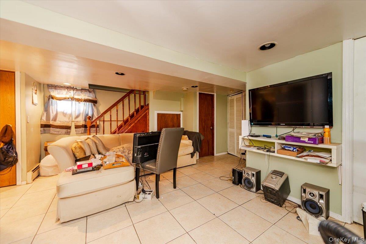 137-27 Thurston Street Queens, NY 11413 - Photo 17 of 19 Living room featuring stairway, light tile patterned floors, and baseboard heating