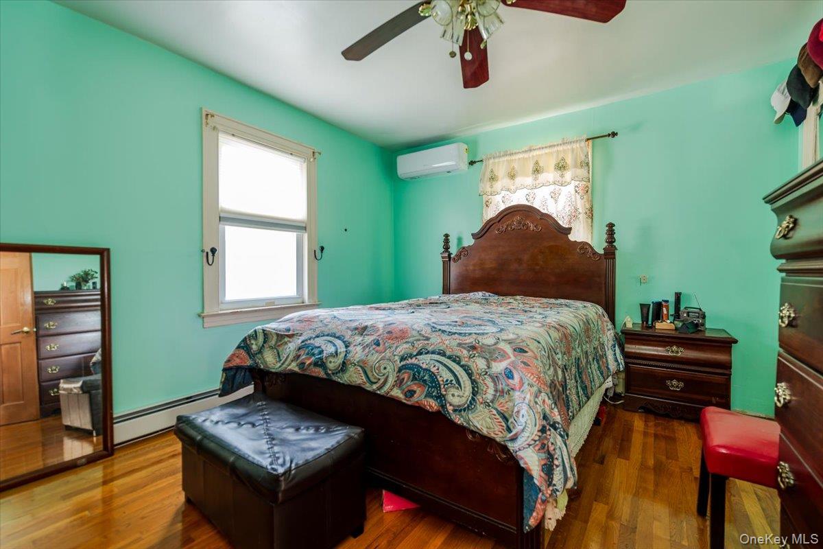 137-27 Thurston Street Queens, NY 11413 - Photo 9 of 19 Bedroom with wood finished floors, a baseboard radiator, ceiling fan, and a wall unit AC