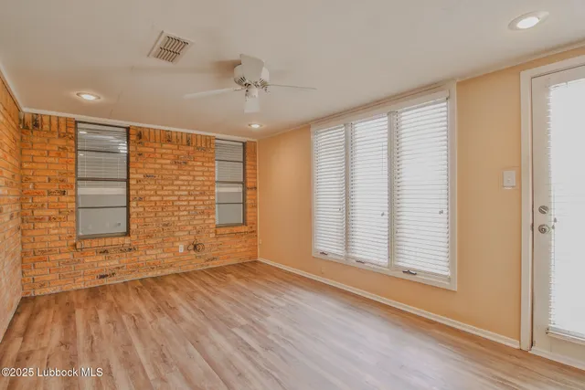 an empty room with wooden floor chandelier fan and windows