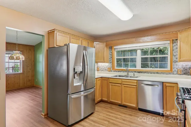 a kitchen with stainless steel appliances a refrigerator a sink a stove and white cabinets with wooden floor
