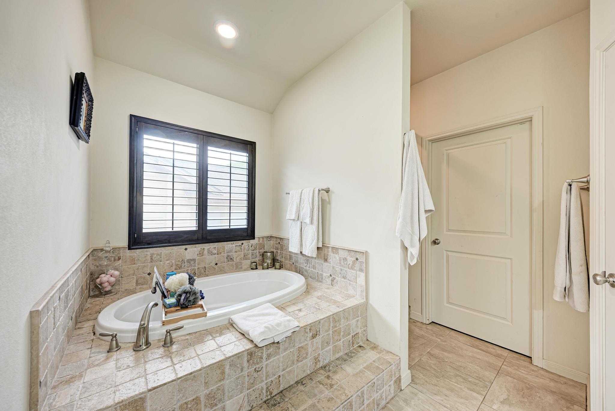 2605 Indian Creek Road Austin, TX 78734 - Photo 15 of 33 Soaking tub with tile surround, brushed nickel fixtures, and plantation shutters