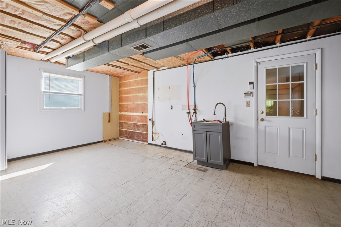1501 Ohltown McDonald Road Mineral Ridge, OH 44440 - Photo 25 of 32 Unfinished room featuring exposed ceiling joists, a utility sink with a dark gray cabinet, white paneled door with glass inserts, and a single window