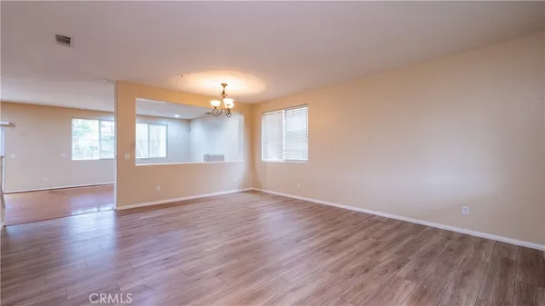 an empty room with wooden floor chandelier and windows