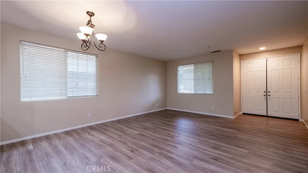 an empty room with wooden floor chandelier and windows