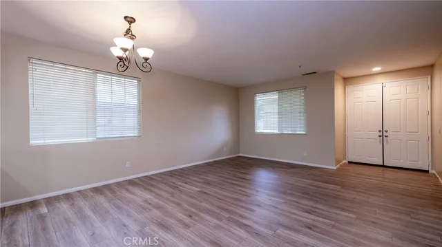 an empty room with wooden floor chandelier and windows